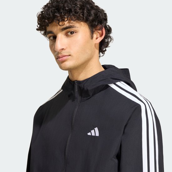 Close-up van zwart Adidas windjack met witte strepen en het Adidas-logo op de borst.