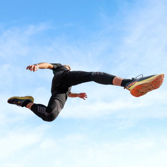 Man in de lucht springend, draagt zwarte sportkleding en zwarte beenstukken met grijs patroon.