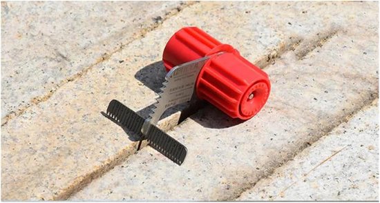 Een rode tape dispenser met metalen snijder en schaalverdeling in een voegen van bestrating.