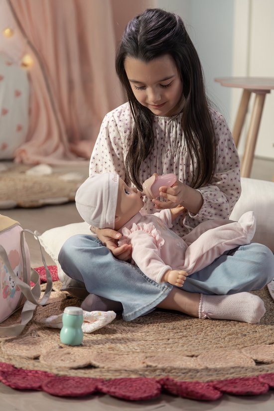 Een meisje geeft een baby-pop in roze kleding een flesje.