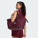Vrouw draagt een bordeauxrode sporttas met zilverkleurig Adidas logo op de schouder.