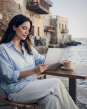 Een vrouw in een lichtblauwe blouse zit aan een tafel met een BOOX e-reader en een kopje koffie.