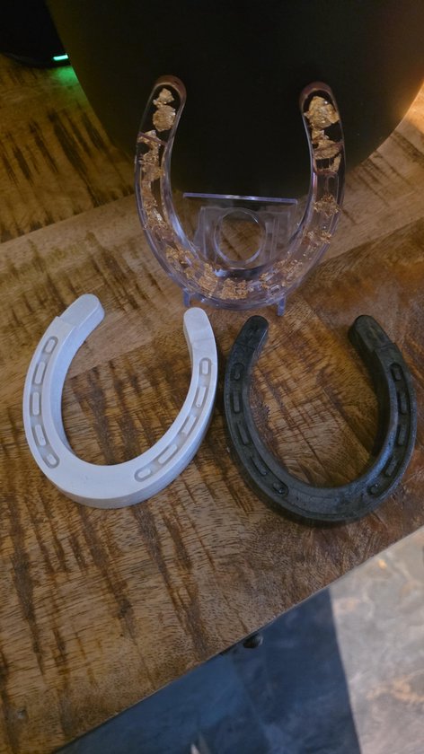 Drie hoefijzers: doorzichtig met goud, zwart en wit, naast elkaar op een houten tafel.
