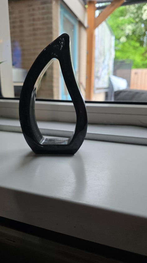 Zwarte, druppelvormige epoxy decoratie met glanzende afwerking, geplaatst op een witte vensterbank met uitzicht naar buiten.