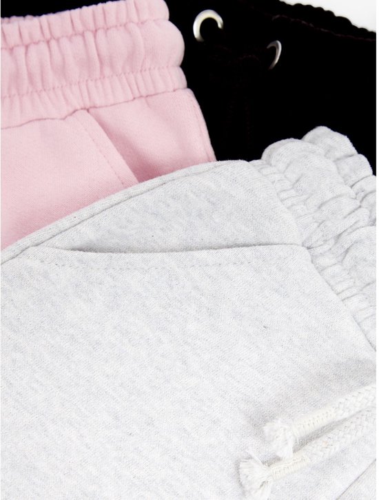 Detail van de taillebanden en zakken van zwarte, roze en lichtgrijze joggingbroeken.
