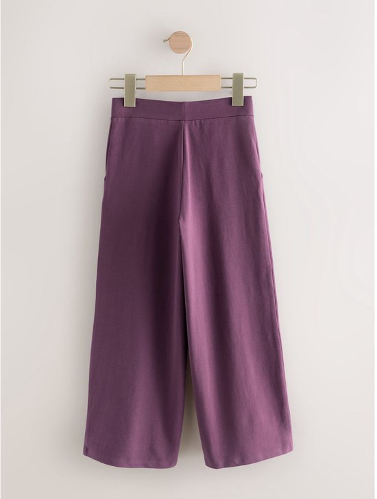 Paarse wijde tricot broek hangend aan een houten kledinghanger.