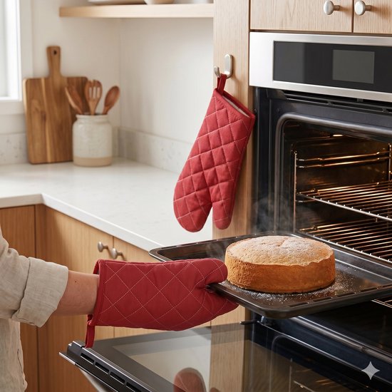 Femme dans une cuisine, retirant un gâteau cuit du four avec des gants de cuisine rouges. De la vapeur sort du four.
