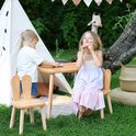 Jongen en meisje spelen bij een houten kindertafel met stoeltjes in de tuin, met een tipi en giraffe knuffel.