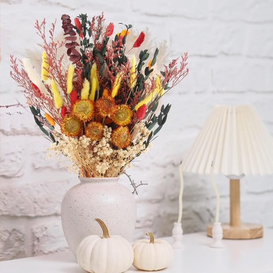Herfstboeket in een gespikkelde vaas met witte pompoenen en een lamp op een tafel.
