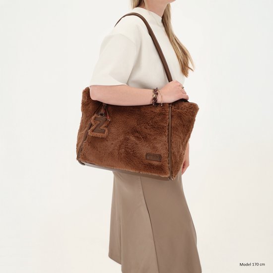 Model draagt een bruine schoudertas van imitatiebont met een 'Z' bag charm, bijpassende armband en bruine kleding.