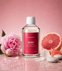 Fles SteamStory "Ruby" wasparfum met roze pioenroos, grapefruit en witte bloemblaadjes op een roze achtergrond.