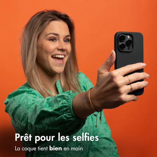 Een lachende vrouw in een groen shirt neemt een selfie met een zwarte telefoonhoes.