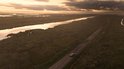 Vogelvlucht van een auto op een landweg die door drassige gebieden slingert bij zonsondergang.