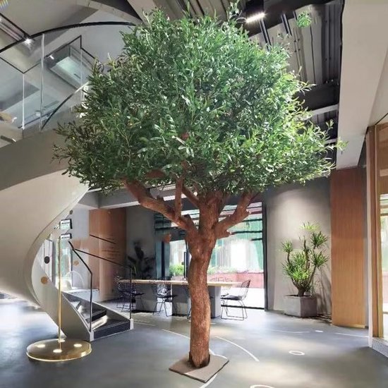 Grote kunstmatige olijfboom met een realistische houten stam en groene bladeren, geplaatst in een moderne woonkamer.