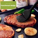 Un pinceau de cuisine en silicone noir est utilisé pour badigeonner un steak sur une plaque de cuisson.