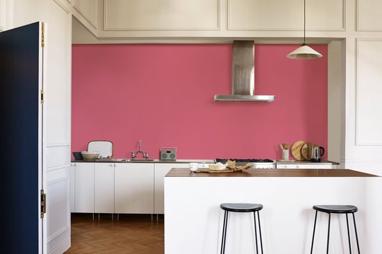 Een keuken met een roze muur, witte kasten, een aanrecht, een kookeiland met barkrukken en kookapparatuur.