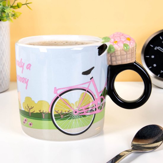Witte mok met roze fiets en bloemenmandje als handvat, gevuld met roze bloemen. Tekst: 'Happiness is only a bicycle ride away'.