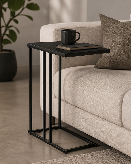 Zwart bijzettafel met metalen frame, staand naast een beige bank. Een mok en boek liggen op het blad.