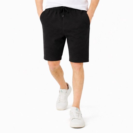Man die een zwarte katoenen short met trekkoord en steekzakken draagt, met witte T-shirt en witte sneakers.