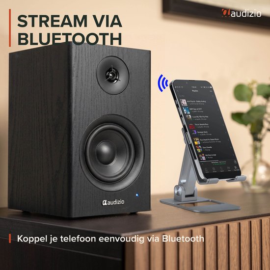 Zwarte houten boekenplank speaker naast een smartphone op een standaard, met tekst 'STREAM VIA BLUETOOTH'.