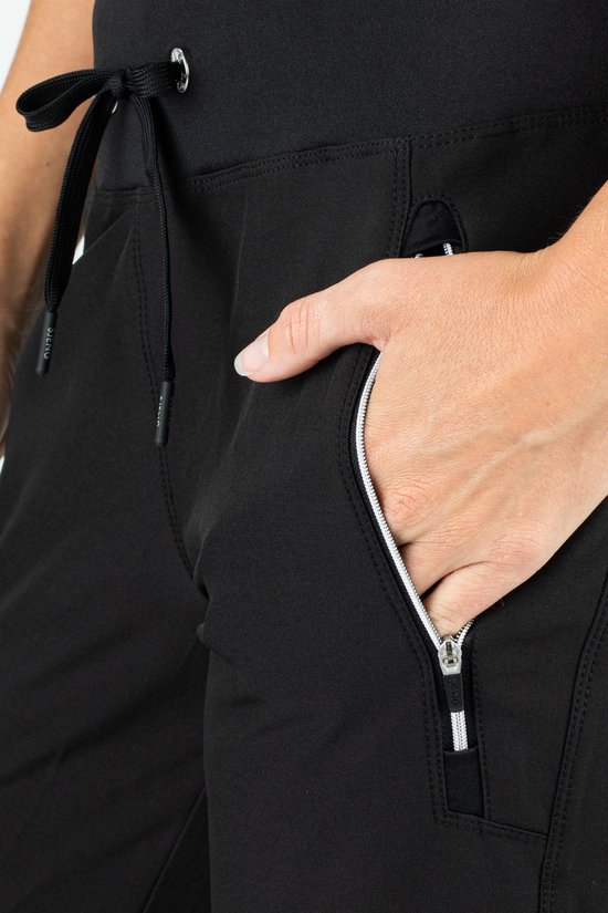 Detail van de zak van een zwarte stretch trainingsbroek, met een rits met witte bies.