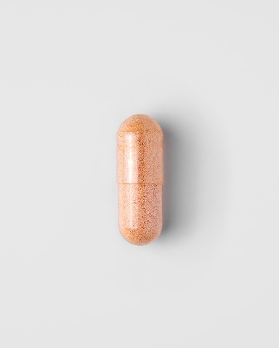 Een enkele oranje capsule met een korrelige textuur, liggend op een witte achtergrond.