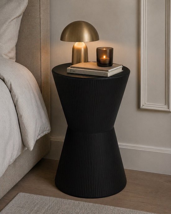 Zwarte bijzettafel met ribbelpatroon naast een bed, met lamp en boeken erop.