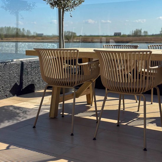 Beige tuinstoelen met ribbelpatroon en metalen poten aan een houten tafel op een houten terras aan het water.