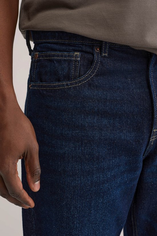 Detail van de voorzakken van een donkerblauwe jeans met gele stiksels.