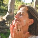 Een vrouw brengt zonnebrandcrème aan op haar gezicht, in de zon, in een bosrijke omgeving.