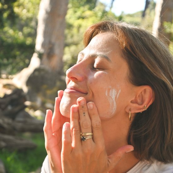 Een vrouw brengt zonnebrandcrème aan op haar gezicht, in de zon, in een bosrijke omgeving.