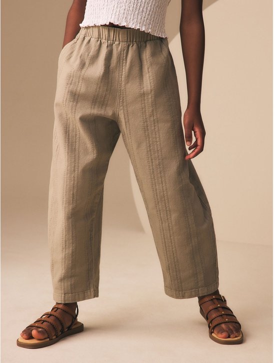 Meisje in een witte crop top en beige broek met verticale strepen, met sandalen.