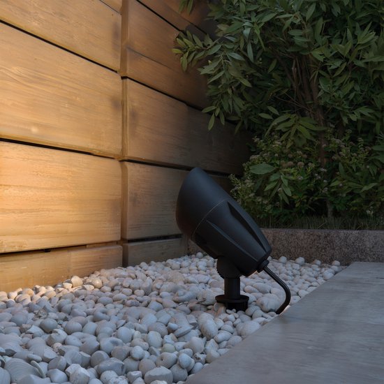 Zwarte prikspot verlicht kiezelstenen en planten naast houten schutting.