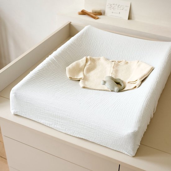 Witte textiel luierkussen met crèmekleurig babyvestje en grijze bijtring.