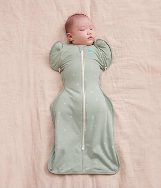 Baby in een sagegroene slaapzak met witte takjesprint en rits, armen omhoog.