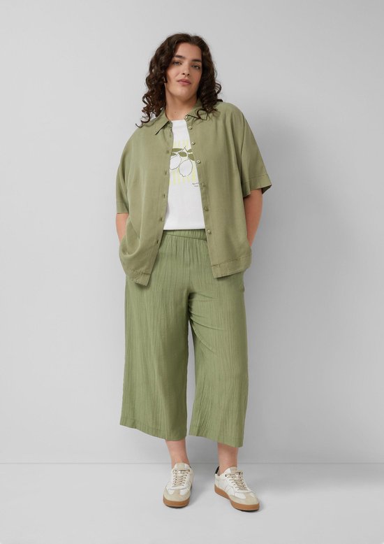 Model draagt olijfgroene culotte met crinkle stof, wit T-shirt met print en bijpassende blouse.