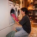 Een man plaatst een rood kersenpitkussen in een wasmachine.