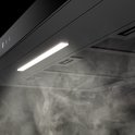 Zwarte afzuigkap met verlichting en opstijgende rook eronder.