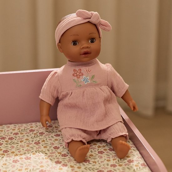 Babypop Yara in roze outfit met bloemenborduursel, zittend.