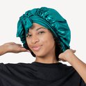 Model met een smaragdgroene satijnen slaapmuts met strik. De muts is gedrapeerd en heeft een zachte glans.