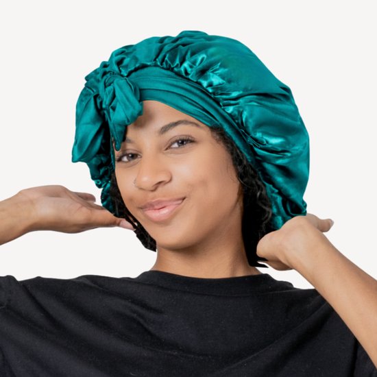 Model met een smaragdgroene satijnen slaapmuts met strik. De muts is gedrapeerd en heeft een zachte glans.