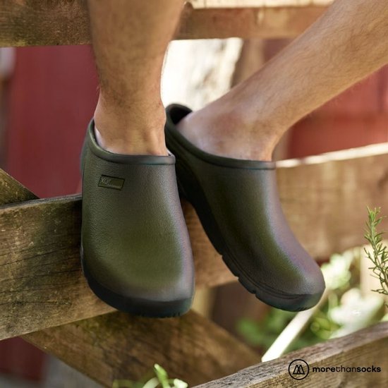 Man op een hek, zittend met groene klompen aan.