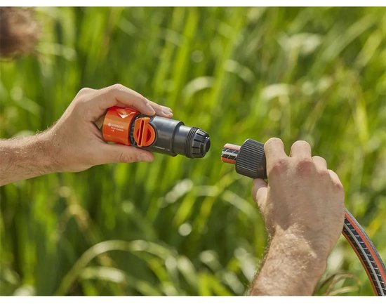 Twee handen verbinden een oranje Gardena Profi System ventiel met een tuinslang.
