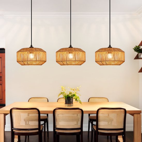 Drie rotan hanglampen met een cilindrisch, geweven design, hangend boven een houten eettafel in een woonkamer.