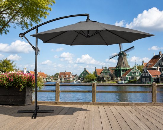Grijze zweefparasol met stalen frame, kruisvoet en molen op de achtergrond.