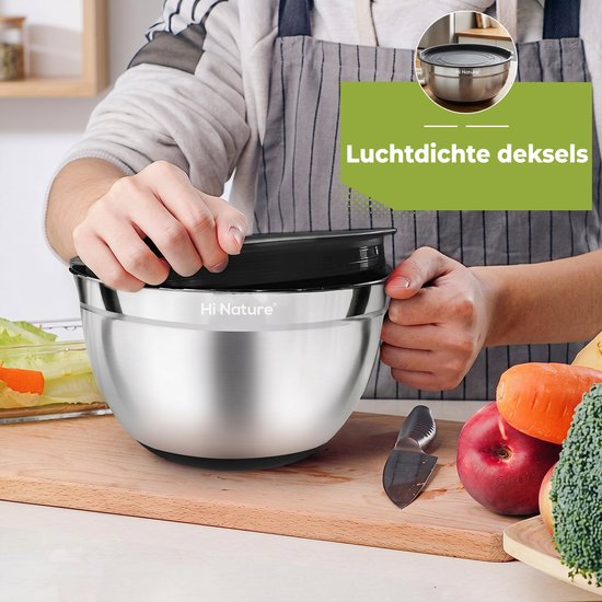 Roestvrijstalen mengkom met zwarte, luchtdichte deksel, omringd door groenten en fruit op een houten snijplank.