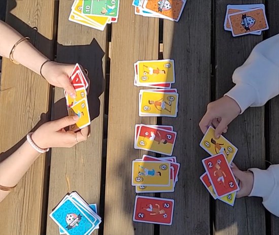 Spelers met handen die speelkaarten vasthouden en neerleggen op een houten tafel.