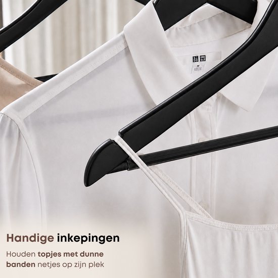 Zwarte houten kledinghangers met inkepingen voor dunne bandjes, hangend aan een wit shirt en een top.