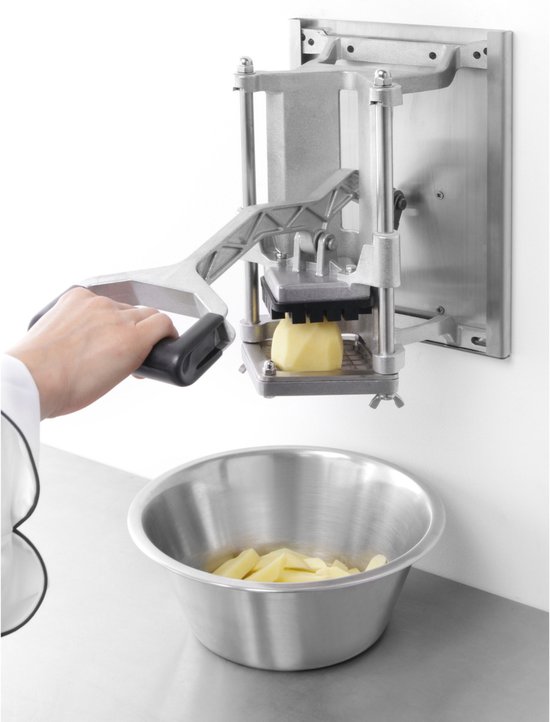 Hand met een chef-kokuniform die een frietsnijder op muurbevestiging bedient, boven een kom met aardappelstukken.