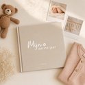 Babyboek 'Mijn eerste jaar' in beige met geborduurde teddybeer, gedroogde bloemen en babykleding.